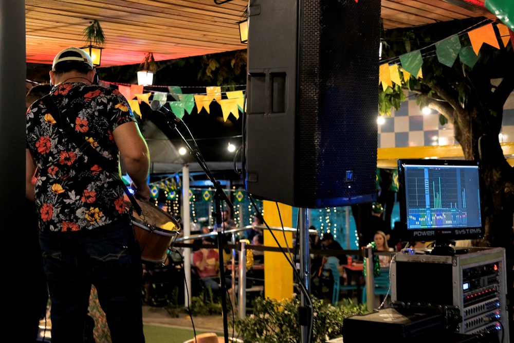 man in floral shirt carrying guitar by PA speaker