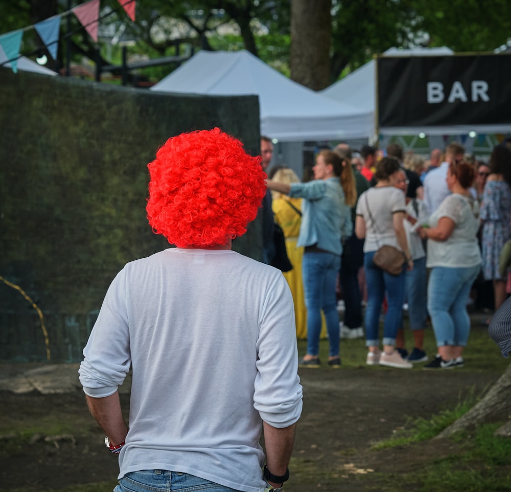 man in white sweat shirt with red wig walking towards bar