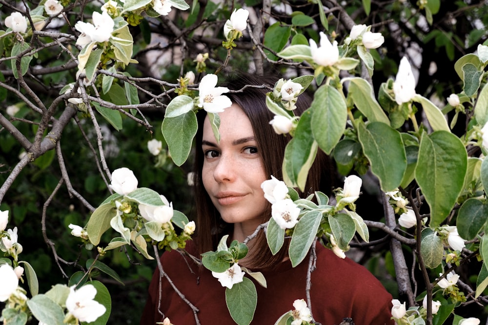 woman in maroon shirt standing behind white flowered bushes