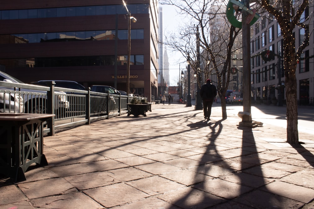 person walking by bare trees by concrete building during daytime