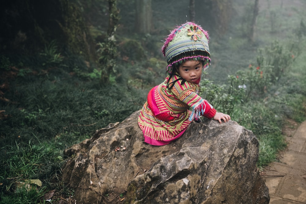 girl in multicolored tribal dress sitting on brown rock