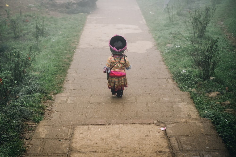 child walking on concrete pathway near green field