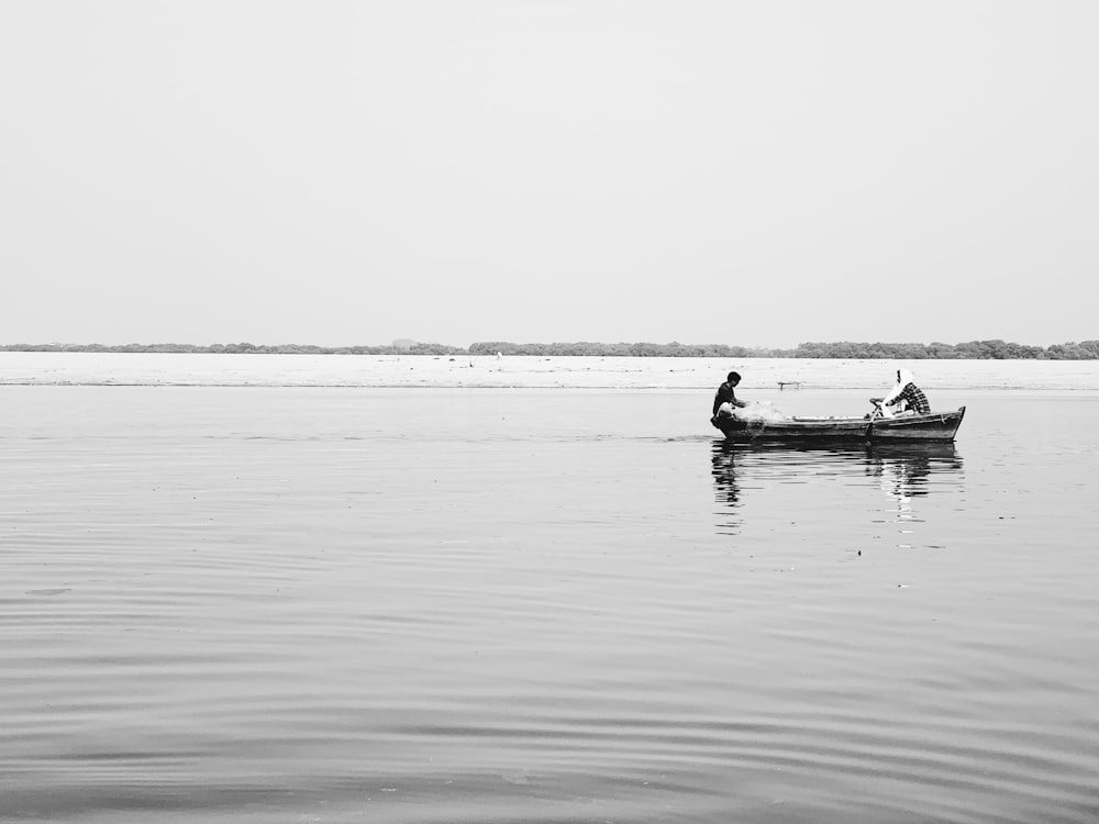 grayscale photography of two people on boat on body of water