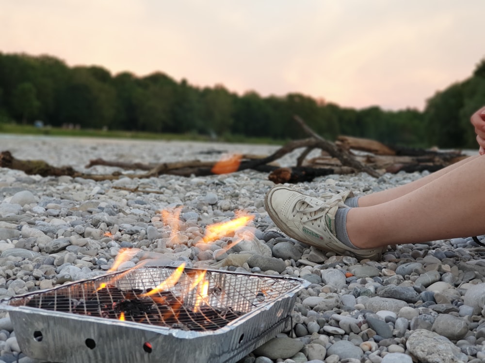 person sitting beside lighted coals in grey grill