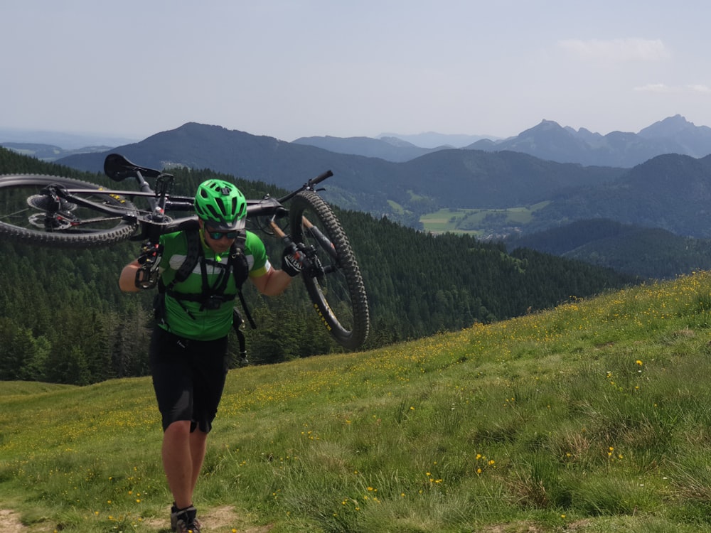 man walking and carrying bike on grass field