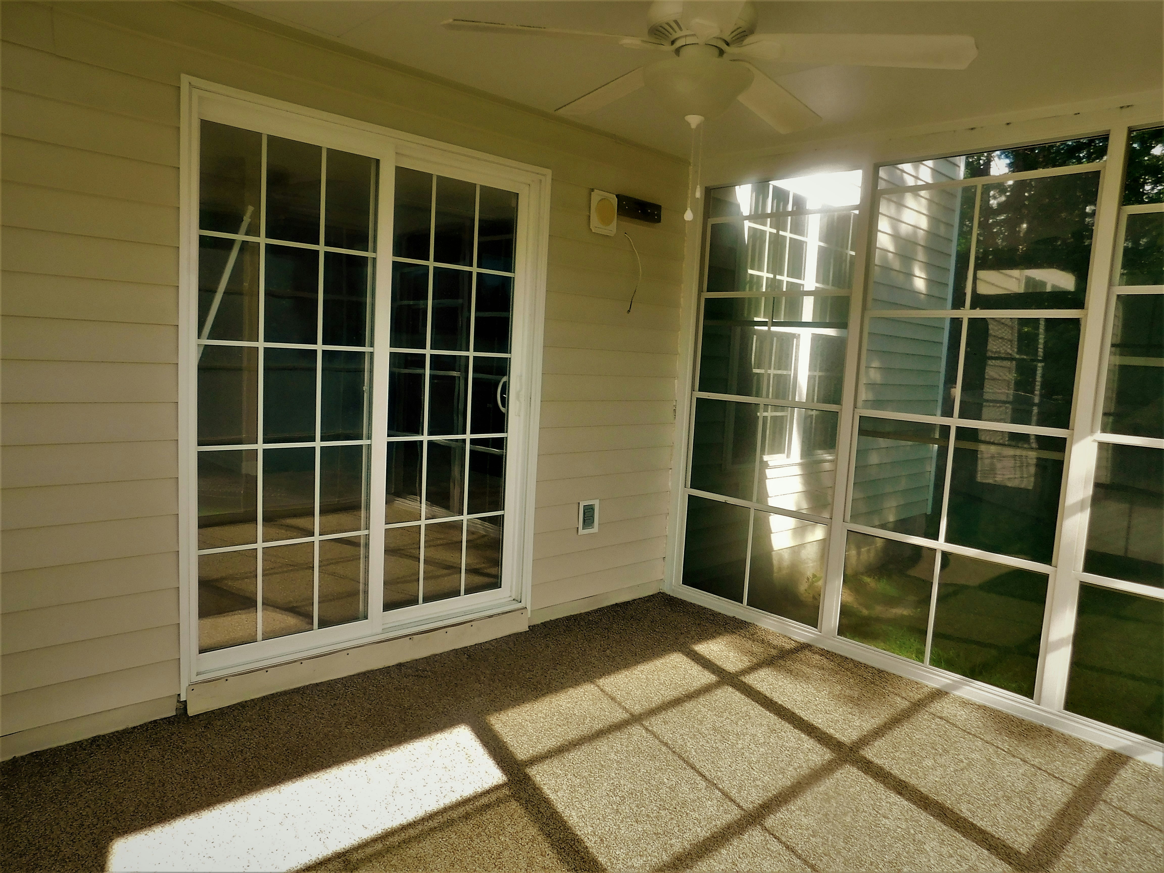 White-framed screened porch with ceiling fan and comfortable lounge chairs, garden view through mesh