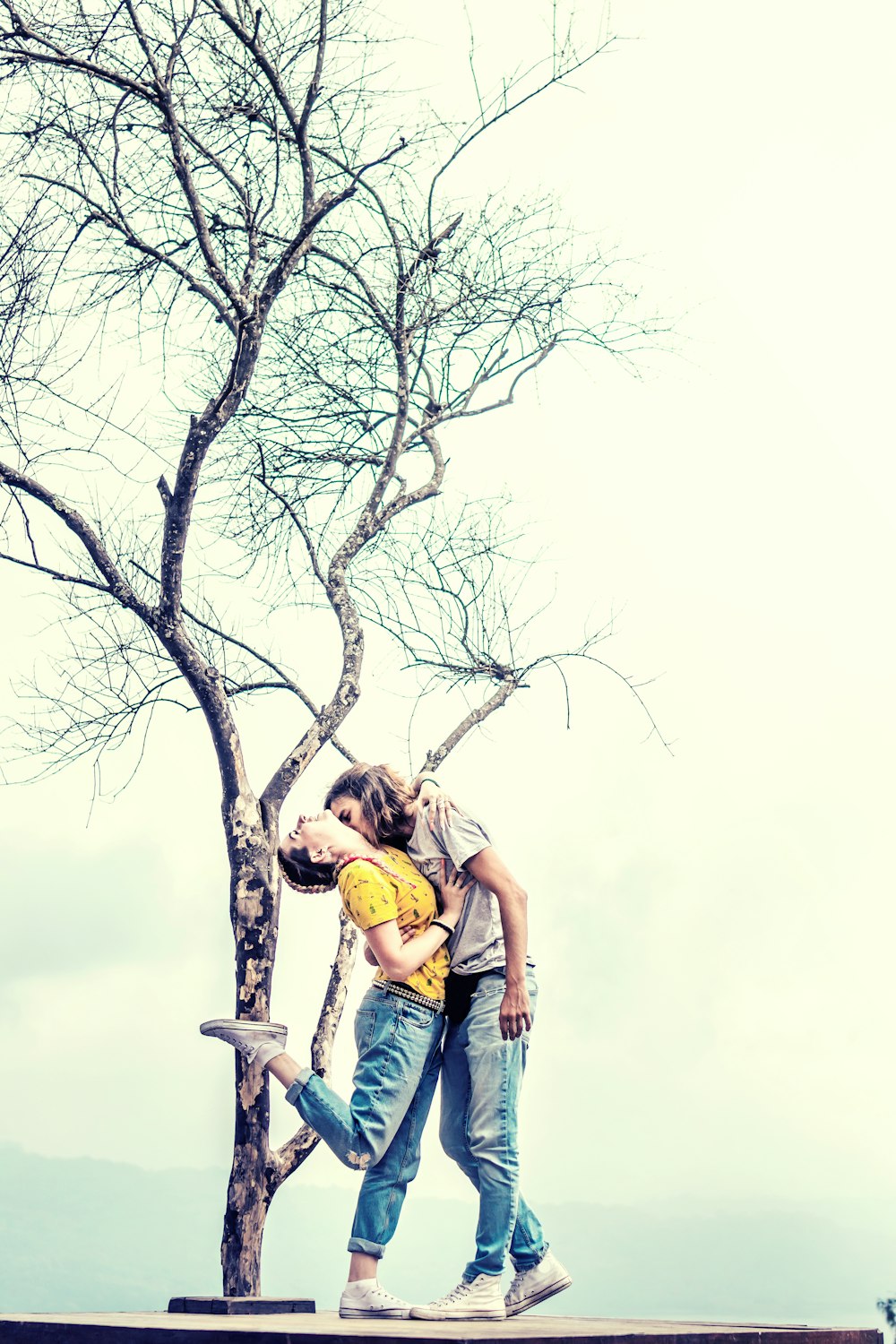 hombre y mujer besándose bajo un árbol sin hojas