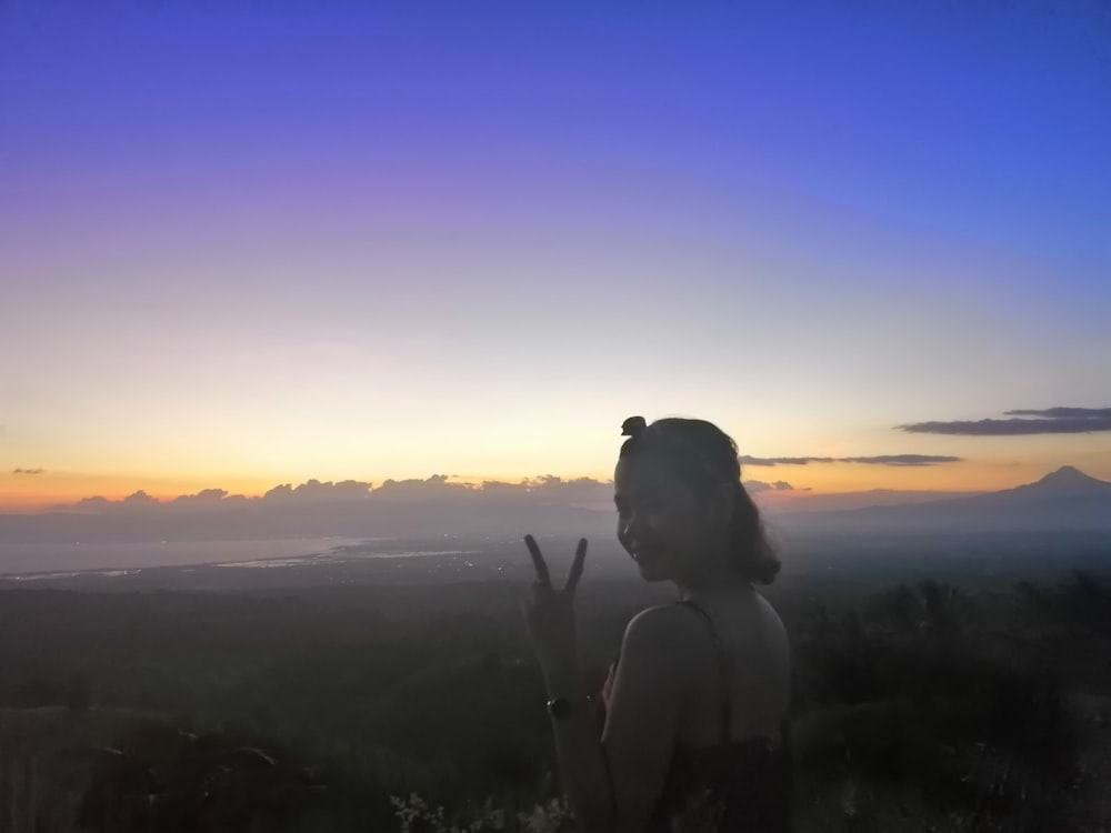 woman making peace hand sign standing on hill