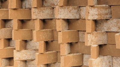 A close-up view of a stack of clay bricks arranged in an interlocking pattern, showcasing their rough texture and earthen color.