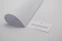 A minimalistic scene with a curved sheet of white paper positioned next to a business card. The business card displays a motivational quote in blue text: 'If you can design one thing, you can design everything.' The card rests on a plain light grey surface.