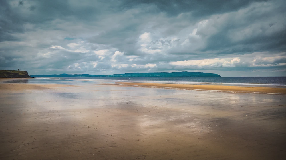 A wide empty beach at low tide under a towering cloudy sky