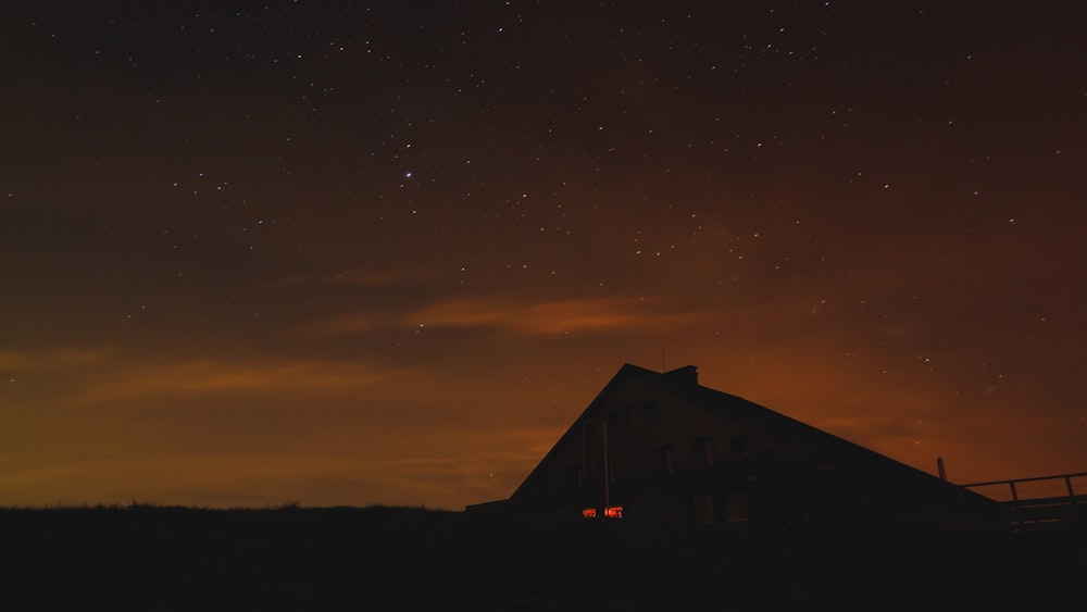 silhouette of cottage under orange sky at night