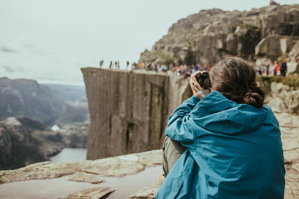 mujer en chaqueta azul tomando foto de personas en la cima de un acantilado con cámara DSLR