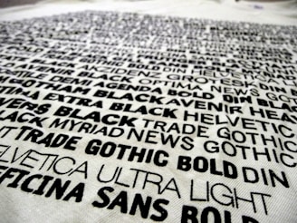 A collection of various fonts and typefaces printed in black ink on a white background, with names like Helvetica, Trade Gothic, and DIN. The text is bold and arranged in a scattered manner, showcasing different font weights and styles.