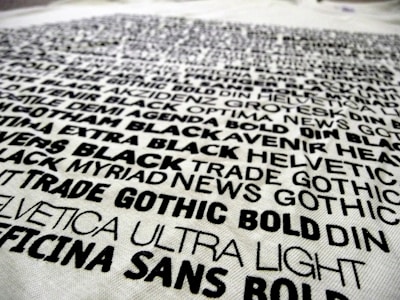 A collection of various fonts and typefaces printed in black ink on a white background, with names like Helvetica, Trade Gothic, and DIN. The text is bold and arranged in a scattered manner, showcasing different font weights and styles.