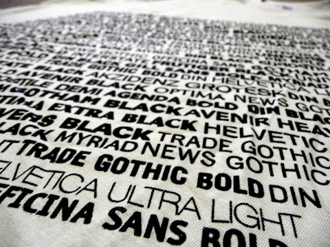 A collection of various fonts and typefaces printed in black ink on a white background, with names like Helvetica, Trade Gothic, and DIN. The text is bold and arranged in a scattered manner, showcasing different font weights and styles.