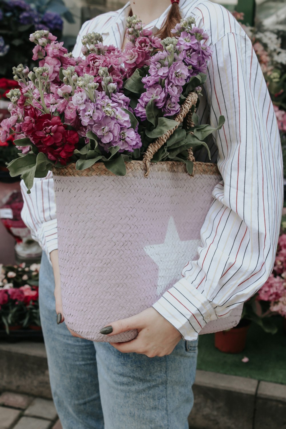 standing woman carrying purple and pink petaled flowers inside basket during daytime