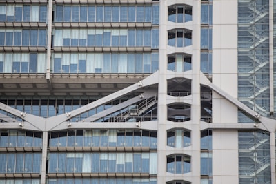 A modern building facade featuring large glass windows and an external steel structure. The structure includes visible diagonal beams and an industrial-style staircase enclosed in glass. The design is symmetrical with clean lines and reflects contemporary architectural elements.