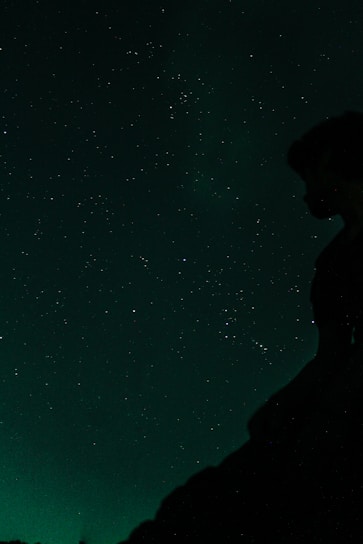 A serene night sky filled with constellations forming a subtle silhouette of a person reaching upward.