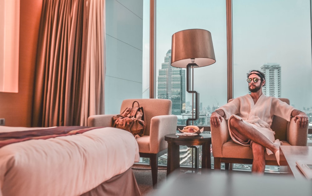 man wearing white bathrobe sitting on sofa chair inside room