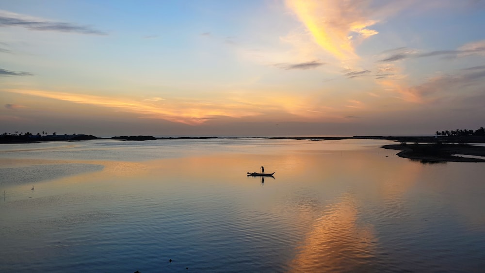 man in boat in under orange sky at sunset