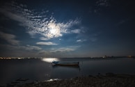 Nighttime shot of a boat illuminated by soft lights, floating peacefully on dark waters.