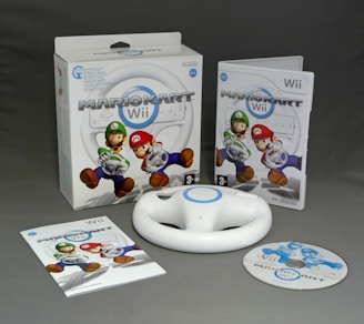 A collection of items related to the game Mario Kart Wii includes the game packaging, a disc, a white steering wheel accessory, and an instruction booklet. The packaging features characters Mario and Luigi.