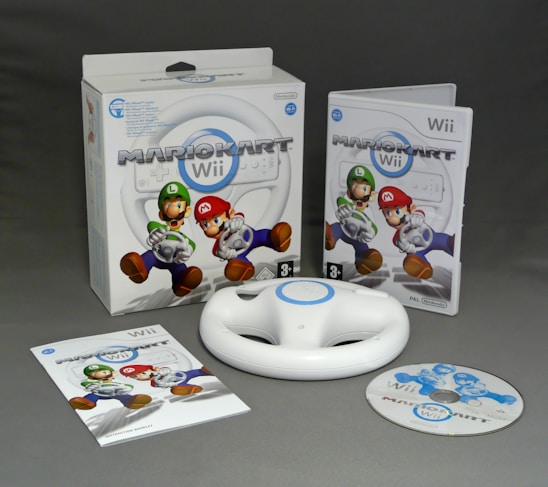 A collection of items related to the game Mario Kart Wii includes the game packaging, a disc, a white steering wheel accessory, and an instruction booklet. The packaging features characters Mario and Luigi.