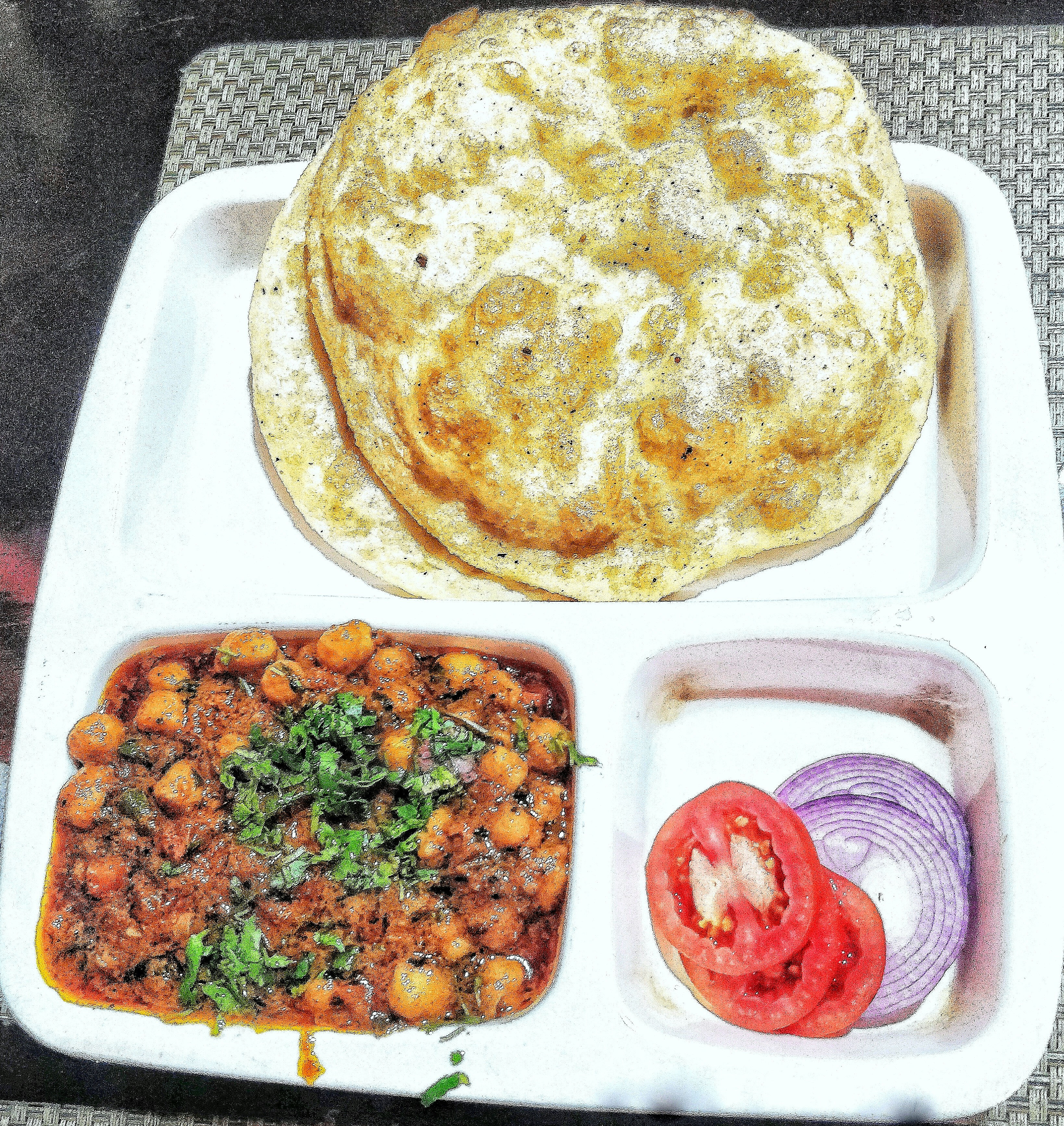 Spicy chole chickpea curry in a dark gravy served with a puffed golden bhatura and sliced onions