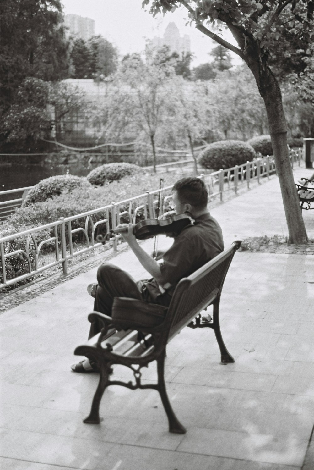 grayscale photography of man playing violin sitting on bench