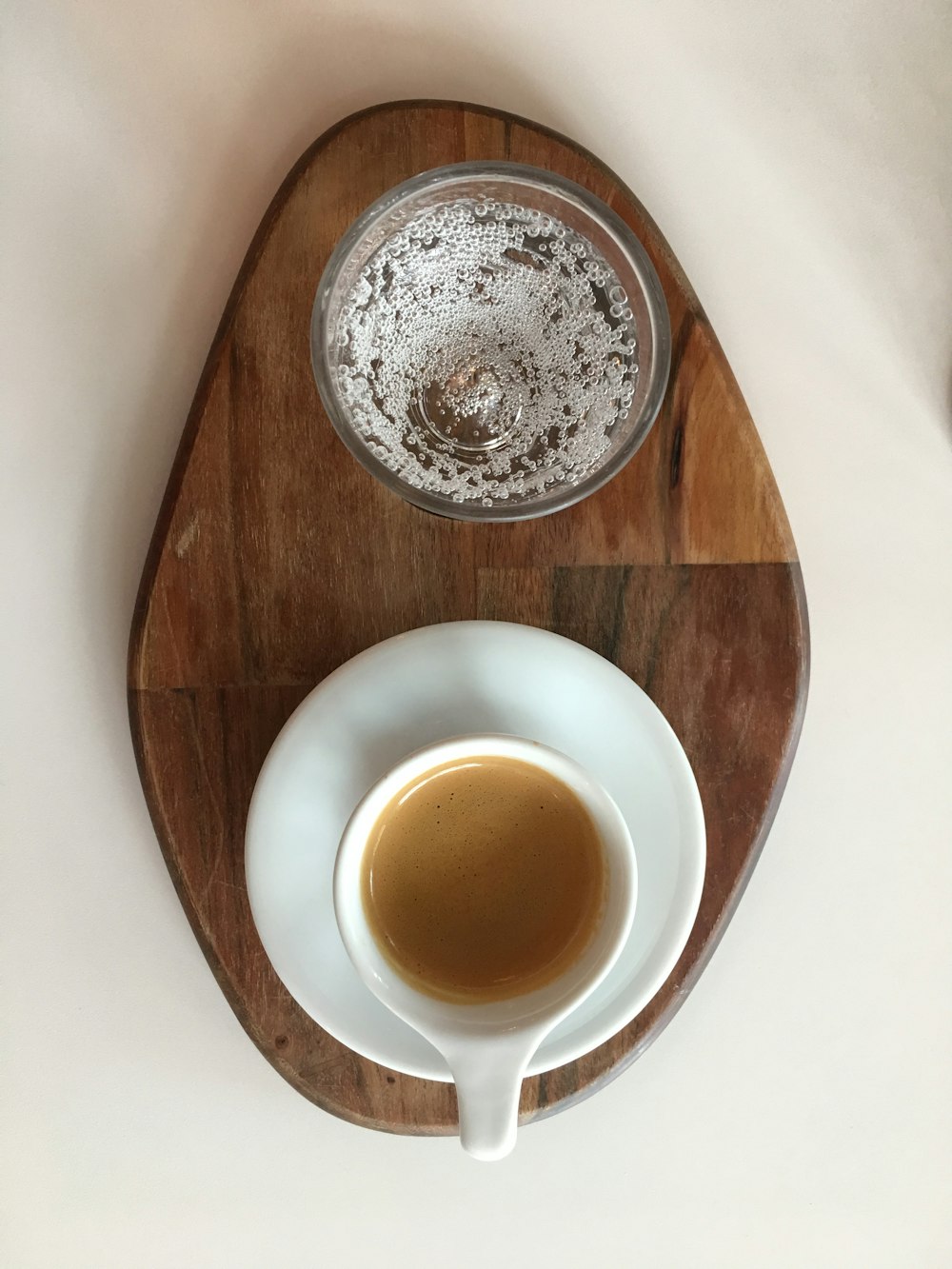 coffee on a white ceramic cup, saucer and clear bowl on a wooden tray