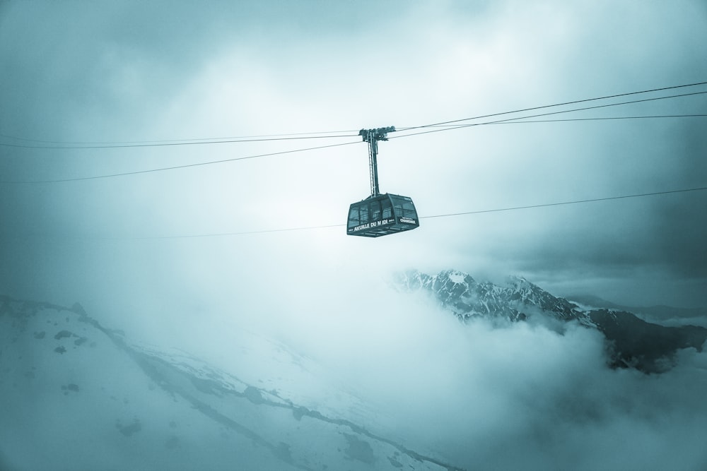 grey cable car traveling above snow covered mountain