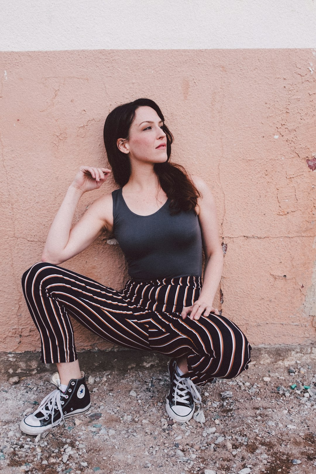 woman wearing black tank top squatting in front of pink wall