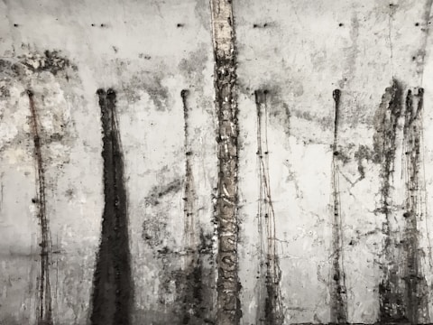A textured concrete wall with vertical streaks and patterns from stains or weathering, giving it an old and industrial appearance.