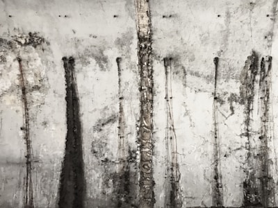 A textured concrete wall with vertical streaks and patterns from stains or weathering, giving it an old and industrial appearance.
