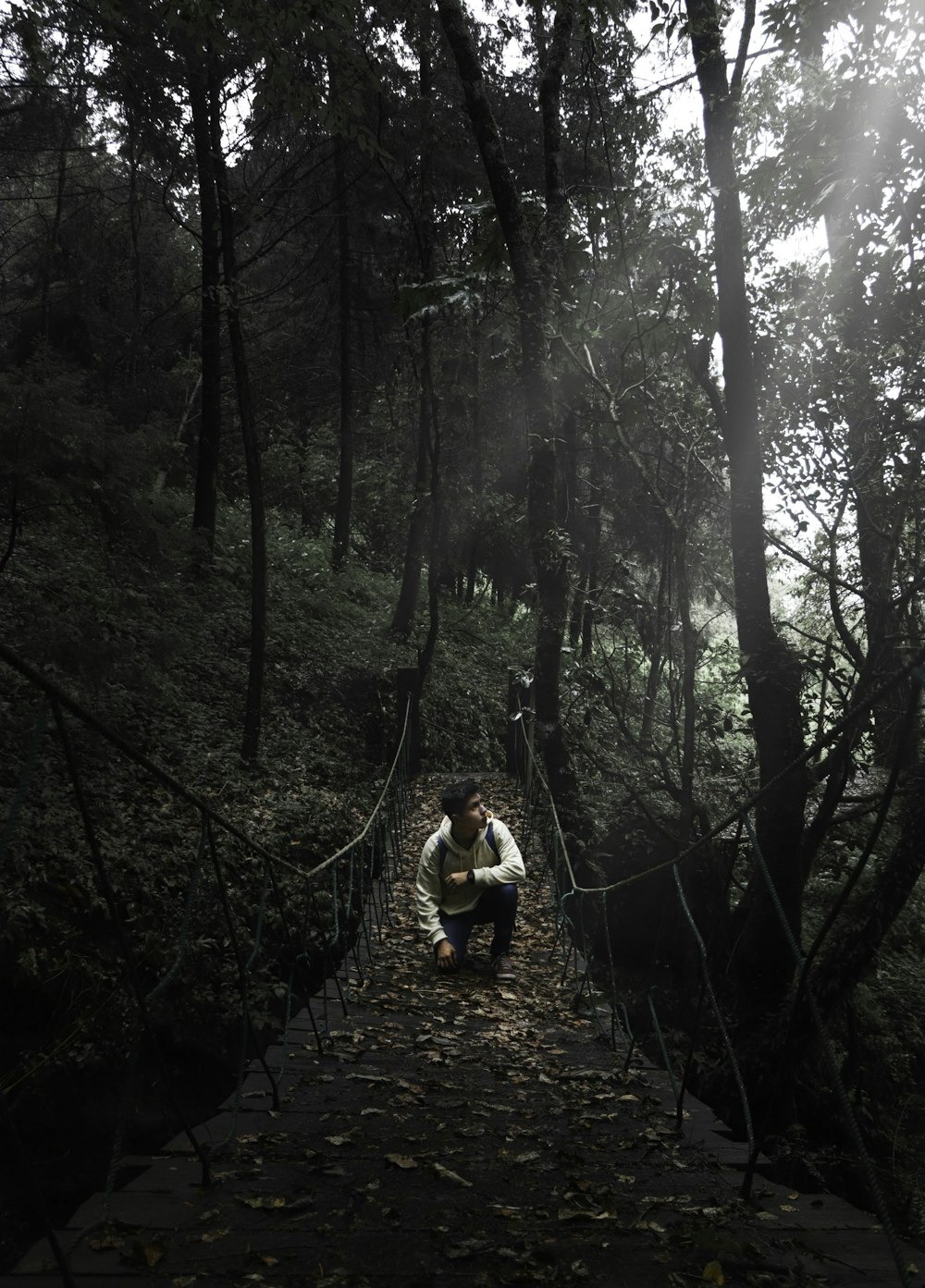 man wearing white dress shirt sitting on brown suspension bridge