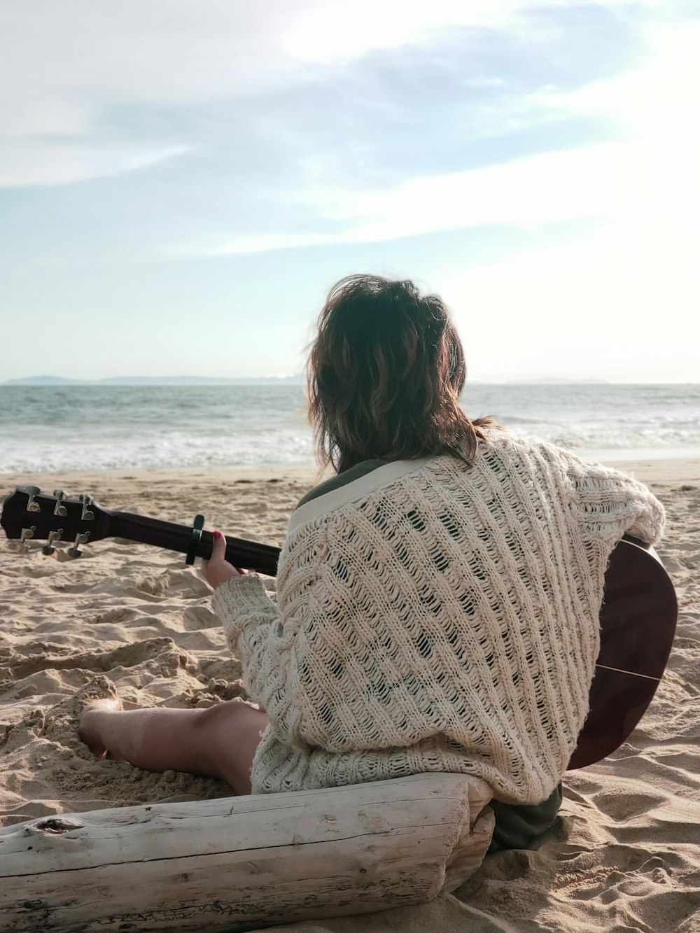 mulher sentada na praia segurando a guitarra