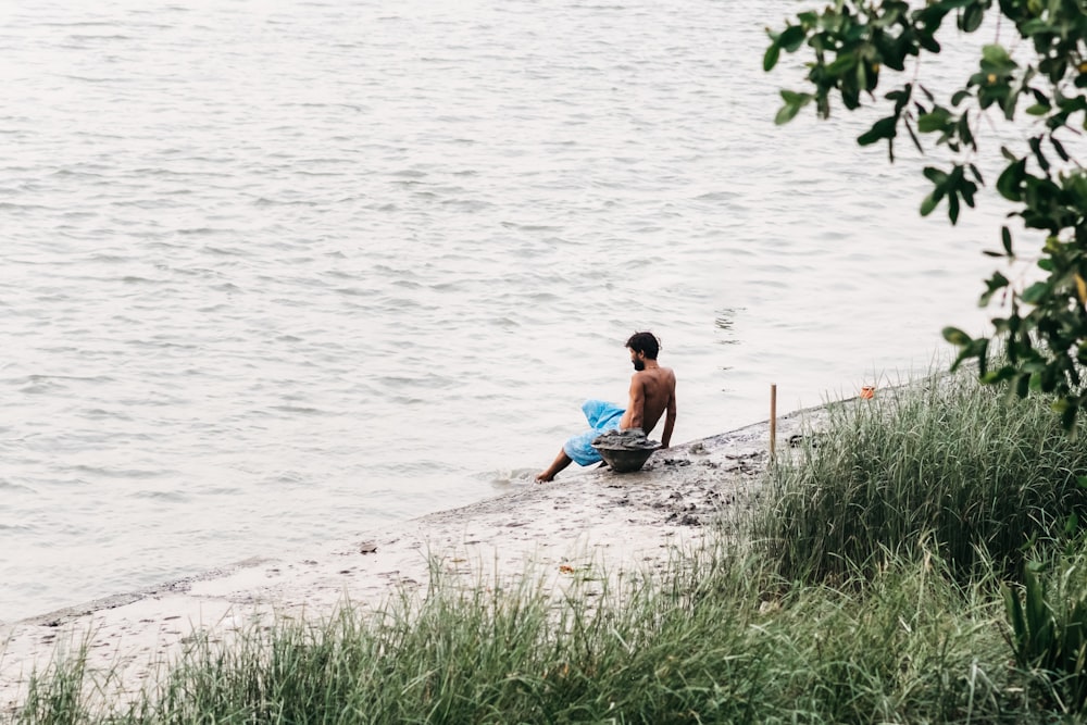 topless man sitting at the shore