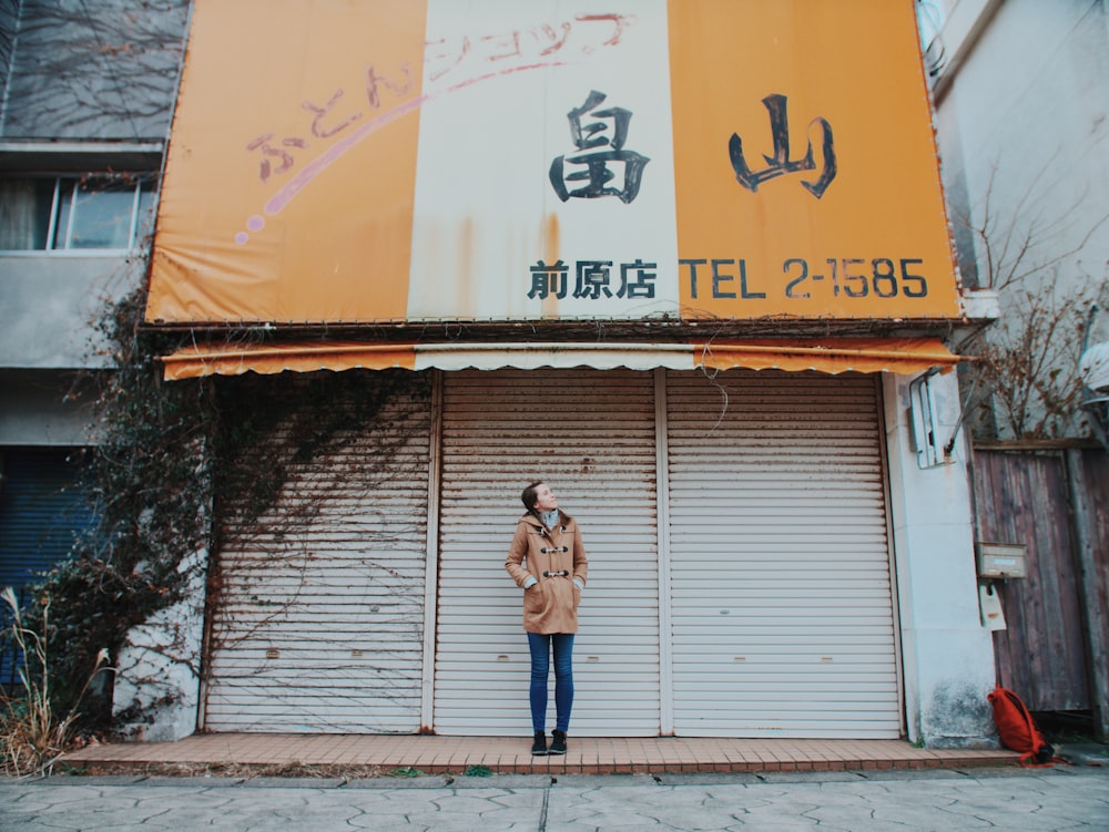 woman wearing beige trench coat standing behind of gray shutter door