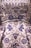 A detailed close-up of an intricately embroidered garment, featuring floral patterns adorned with silver and blue beadwork. The fabric is satin-like, with a lustrous sheen giving it an opulent appearance. The embroidery is rich in detail, combining swirling designs with symmetrical flower motifs.