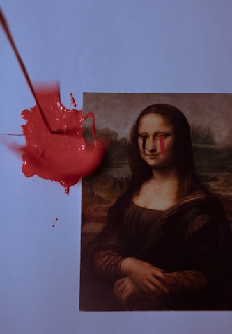 A print of the Mona Lisa is altered with red and blue paint streaked from the eyes. A splash of bright red paint is spread across the top left of the print.