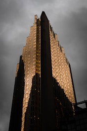 A towering commercial skyscraper with reflective glass and gold trim against a deep black sky.