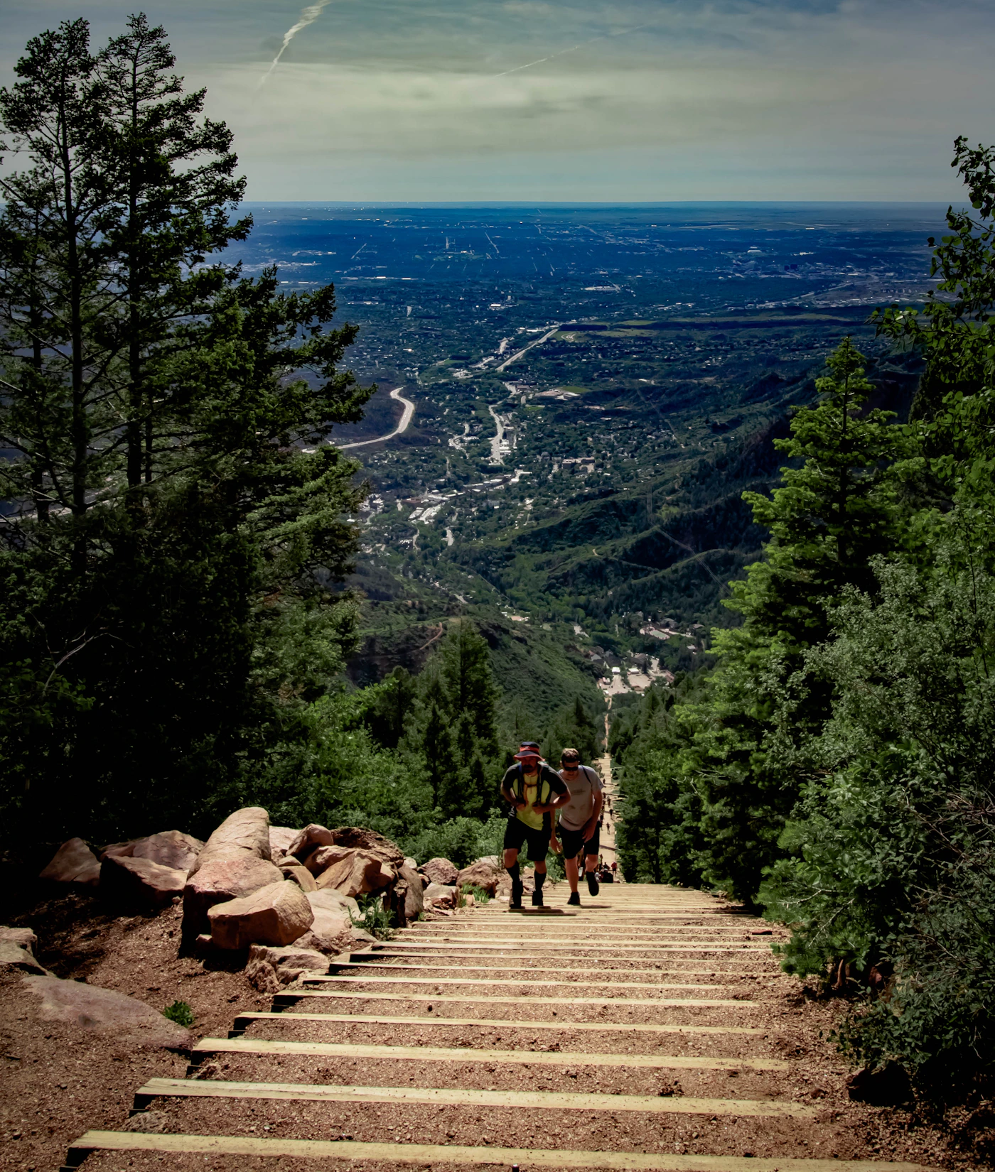 Hikers ascending Manitou Incline timber stairs above the Colorado Springs valley