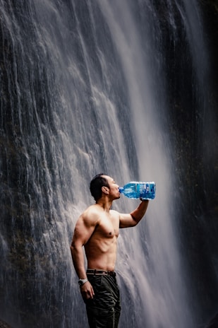 man drinking water beside waterfalals