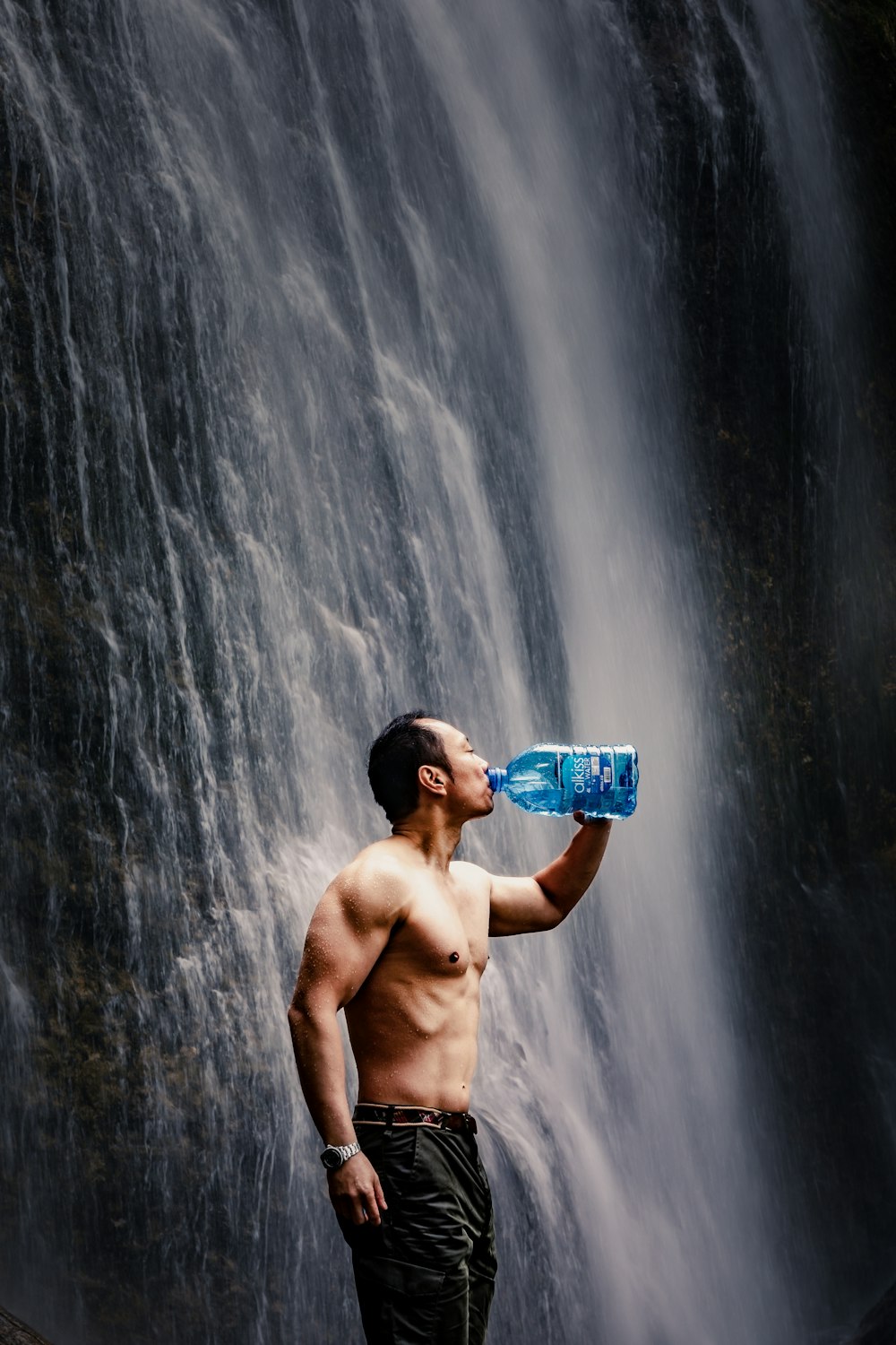 man drinking water beside waterfalals