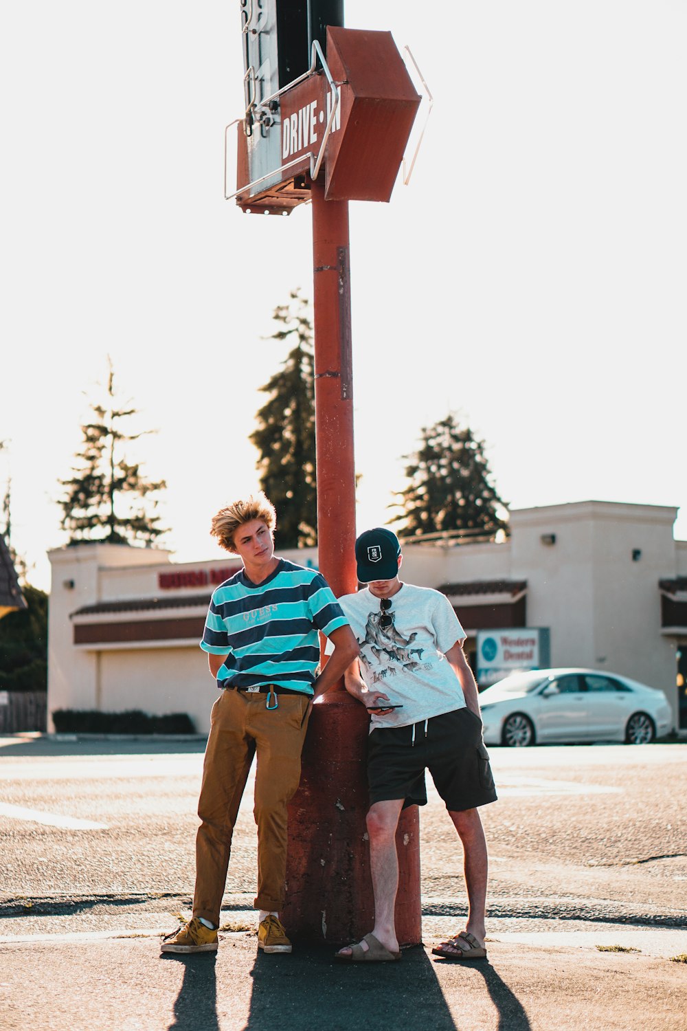 two man standing and both leaning on red metal post