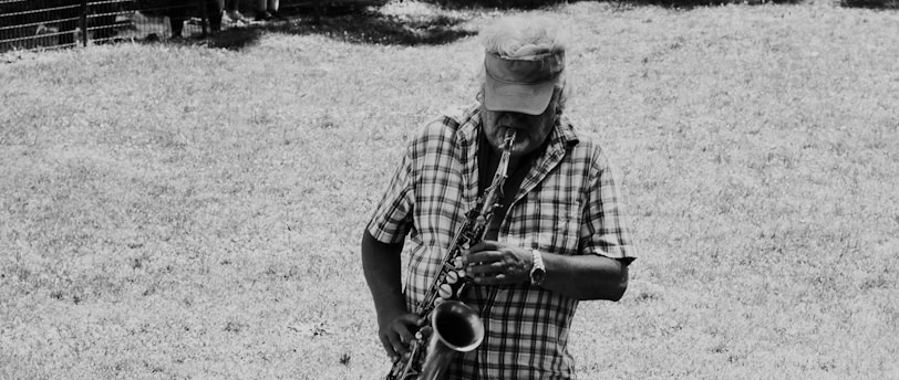 man playing saxophone on grass near trees
