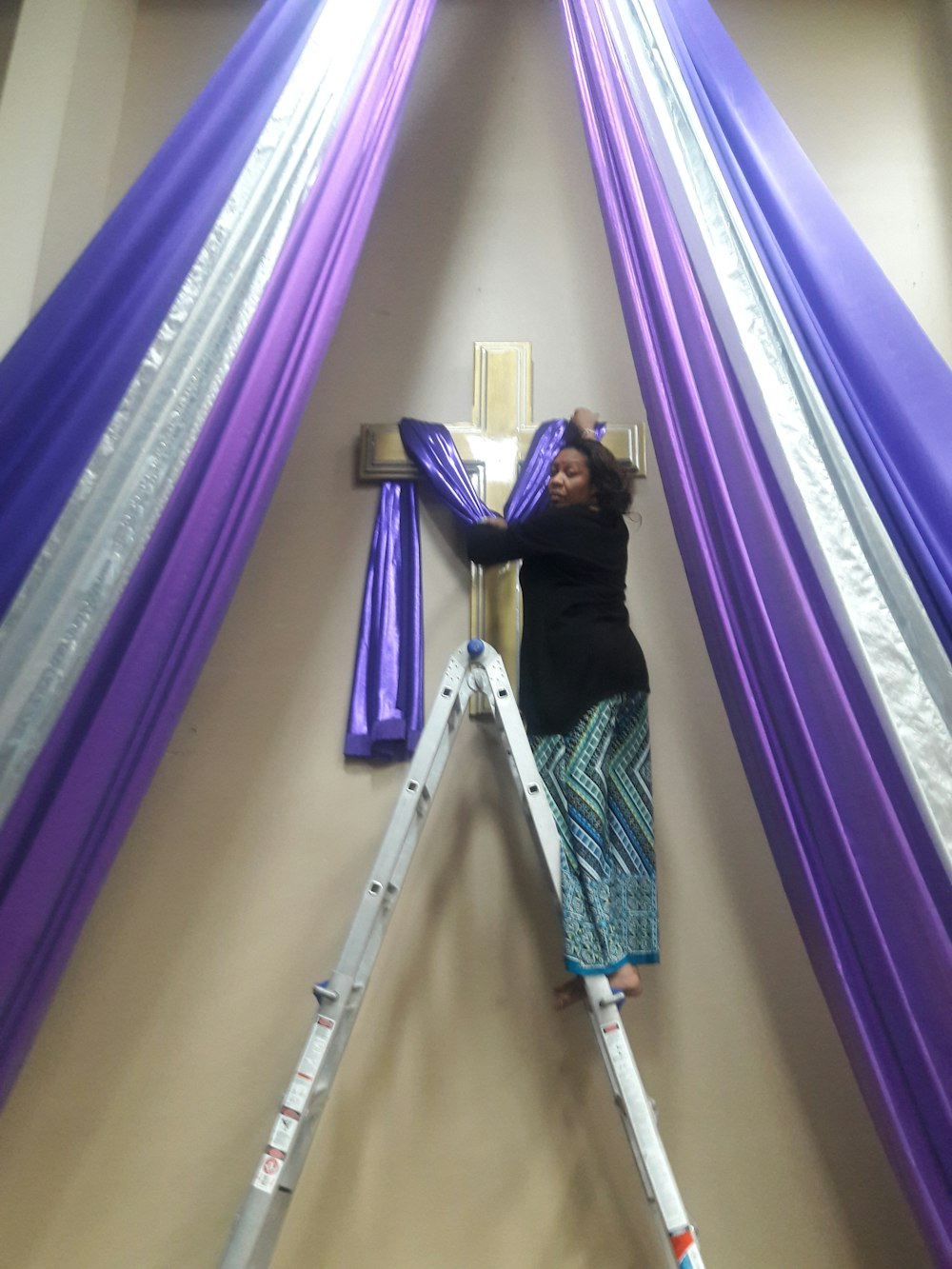 woman on a-frame ladder holding blue textile on wall cross