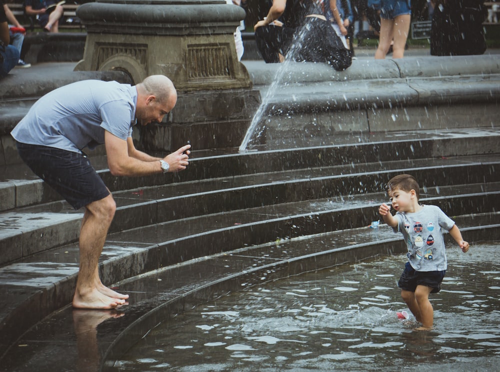 man taking photo of boy standing and playing on on near water fountain