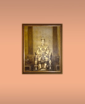 A sepia-toned painting of a regal figure seated on an ornate throne. The figure is adorned with traditional, intricate attire and a headdress, indicative of royalty. The background showcases detailed architectural elements with symmetrical patterns.